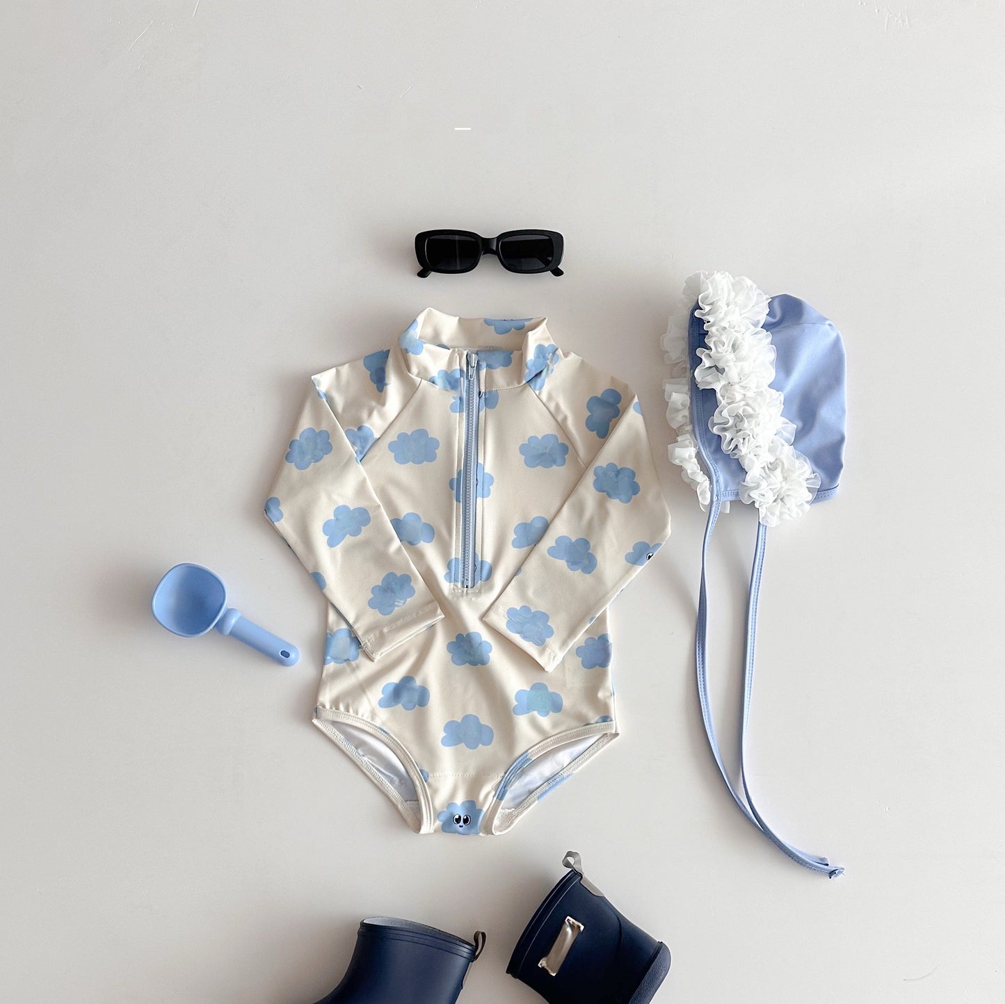 Children's swimsuit with cloud pattern, sunglasses, and accessories on a light gray background