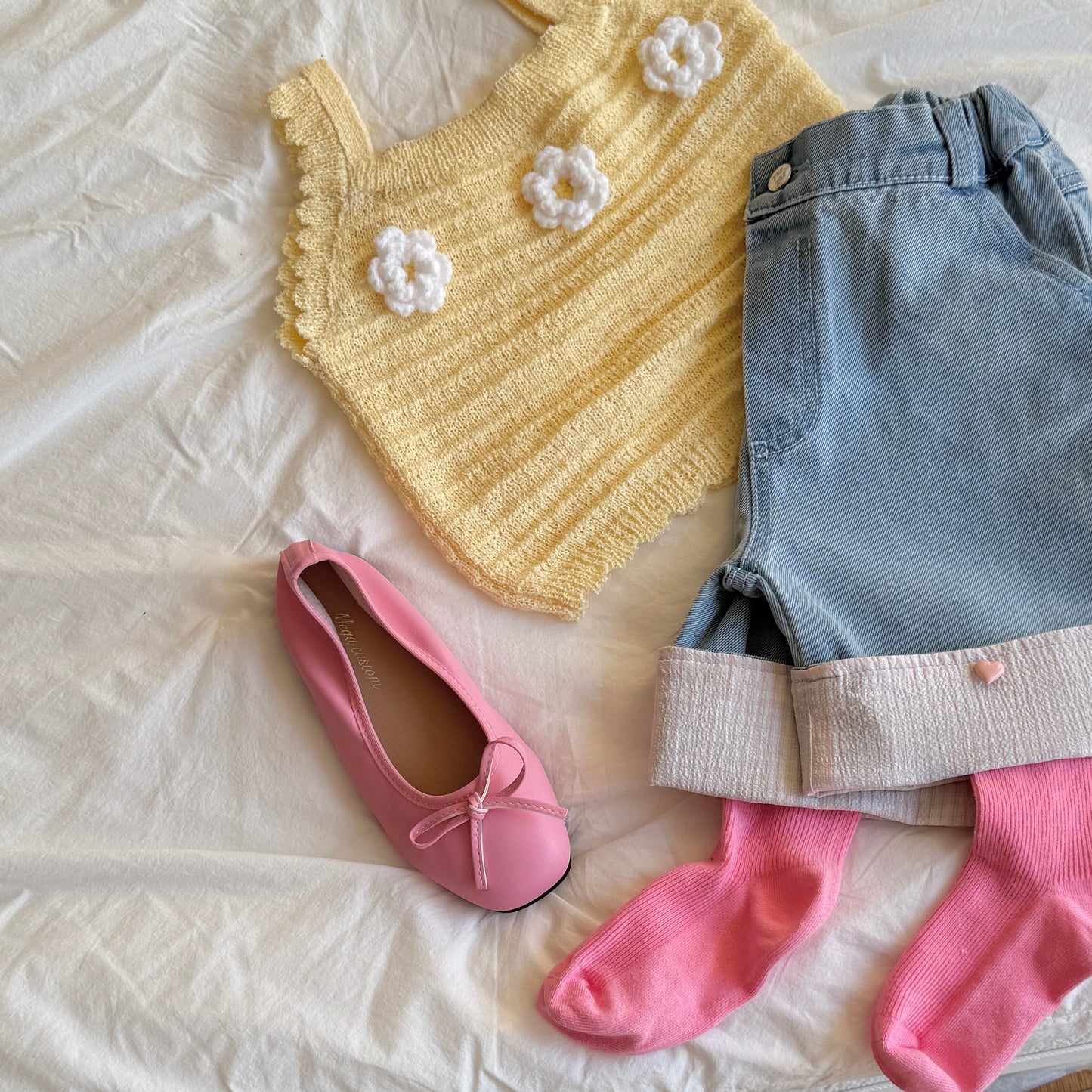 Children's outfit with yellow floral knit top, denim shorts, pink shoes, and socks
