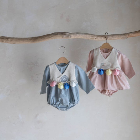 Two Korean baby hanboks hanging on wooden hangers against a plain wall.